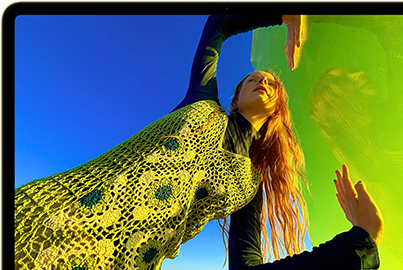 MacBook Neo, สีซิตรัส, หน้าจอแสดงภาพบุคคลที่กำลังยิ้มแย้มและนอนอยู่ในทุ่งดอกไม้ที่มีแดดจ้า