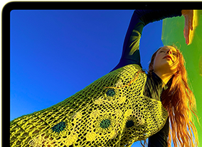 MacBook Neo, สีซิตรัส, หน้าจอแสดงภาพบุคคลที่กำลังยิ้มแย้มและนอนอยู่ในทุ่งดอกไม้ที่มีแดดจ้า