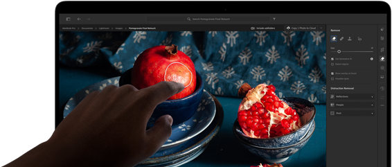 MacBook Pro พร้อมจอภาพ PROLED XDR แสดงภาพนิ่งของผลทับทิมพร้อมเซรามิกและสิ่งทอสีฟ้า มือหนึ่งยื่นออกไปที่หน้าจอเพื่อโต้ตอบกับภาพ